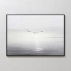“Into the Light Canvas Art – Horizontal” is a framed minimalist wall art print featuring a black and white seascape with five birds flying above calm water and a soft, hazy horizon—ideal for living room decor.