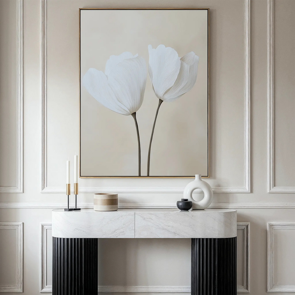 Minimalist decor shines in this neutral-toned interior, featuring a marble console table with vases and candles. Above, the Ivory Buds Canvas Art—a large framed floral artwork—hangs against paneled beige walls.