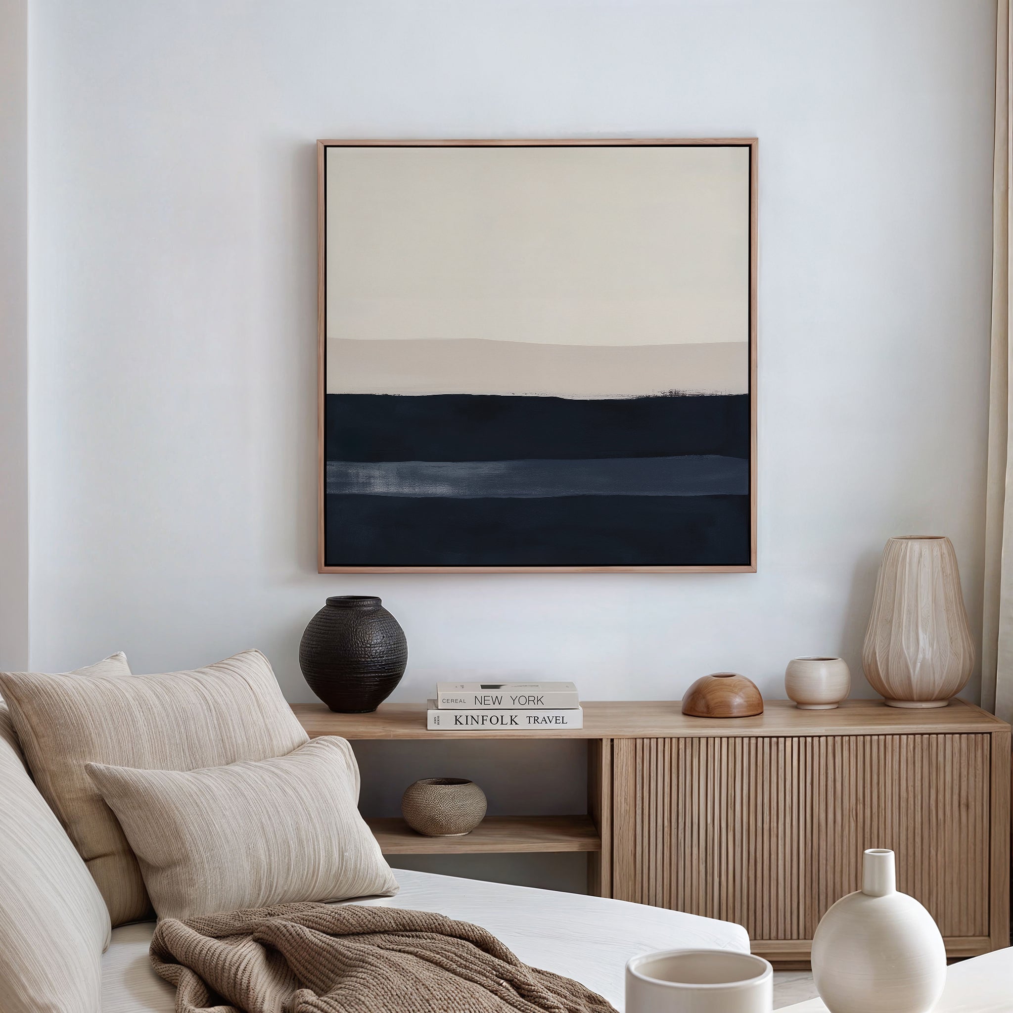 A minimalist living room with a beige sofa, neutral pillows, a wooden sideboard topped with vases and books, and modern interiors accented by the Ivory Dusk Canvas Art featuring muted horizontal bands on a white wall.