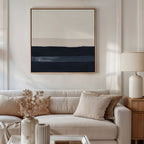 A beige sofa with neutral pillows sits in a modern living room. Above the sofa hangs the Ivory Dusk Canvas Art in cream, taupe, and navy. A lamp and dried flowers adorn a wooden side table nearby.