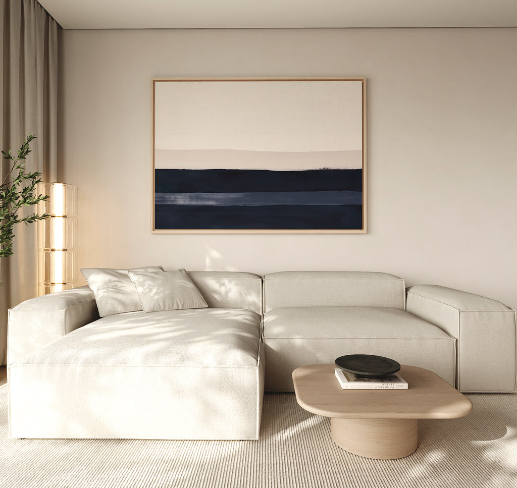 A modern living room with a light beige sectional, low wooden coffee table with a black bowl, Ivory Dusk Canvas Art – Horizontal in blue and beige tones on the wall, and a tall plant by sheer curtains—ideal for stylish decor.
