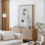 A minimalist living room features a light wood sideboard with neutral decor, ceramic vases, a small green plant, stacked books, and the striking Ivory Mane Canvas Art—a large white horse print hanging above.