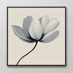 The Ivory Petal Canvas Art features a single flower with soft grey and white petals on a cream background, framed in black—ideal as minimalist floral wall art or elegant bedroom decor.