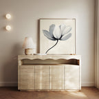 A minimalist console table with a wavy edge displays a lamp, candles, and decor, while the Ivory Petal Canvas Art leans against a light beige wall illuminated by two round wall lights.