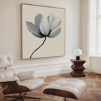 A modern living room with a white leather lounge chair, ottoman, geometric wooden side table with small lamp, and the Ivory Petal Canvas Art featuring soft gray petals—ideal for those who appreciate minimalist wall art.