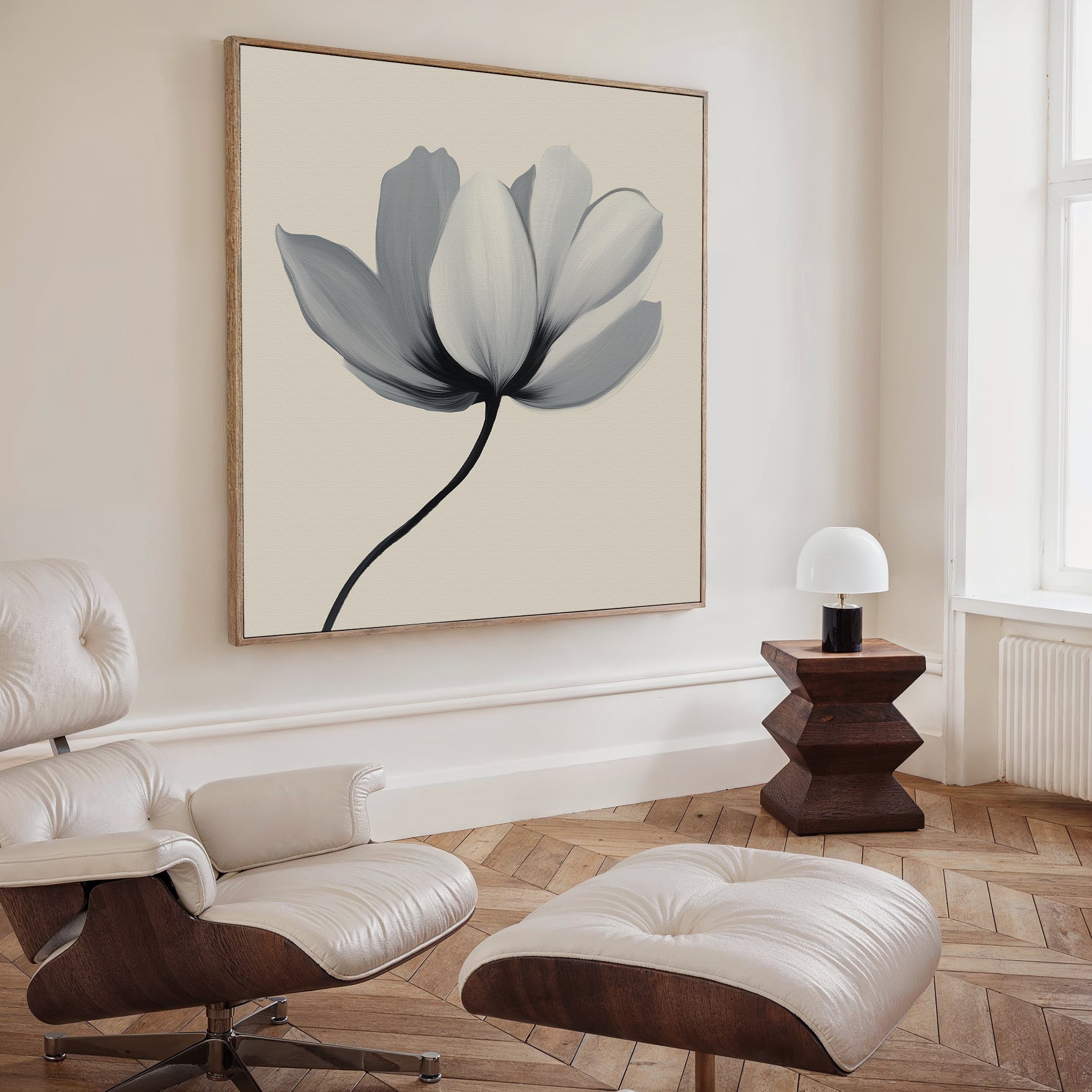 A modern living room with a white leather lounge chair, ottoman, geometric wooden side table with small lamp, and the Ivory Petal Canvas Art featuring soft gray petals—ideal for those who appreciate minimalist wall art.