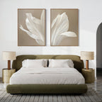 A modern bedroom with a low olive-green bed frame, white bedding, two beige nightstands with matching lamps, and minimalist wall art—the Ivory Petals Set of 2 featuring white flowers displayed above the bed.