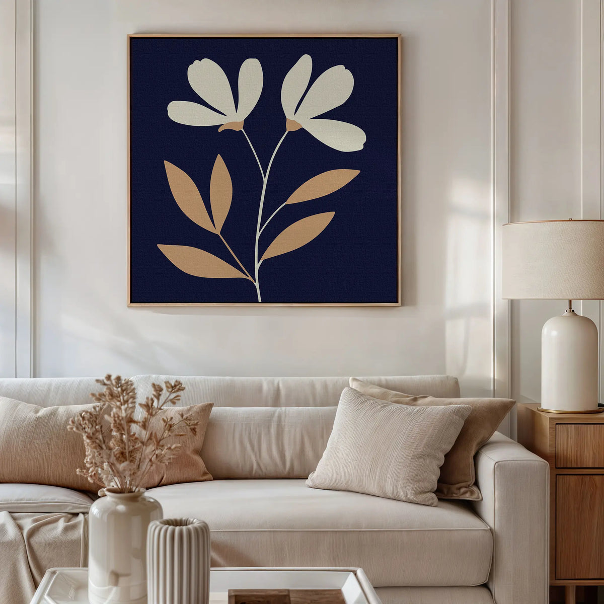 A modern living room with a beige sofa, neutral cushions, dried flowers, a table lamp, and the Ivory Stems Canvas Art featuring minimalist ivory stems and tan leaves on a dark blue background.