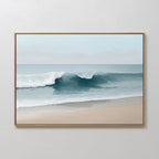 The Lapping Tide Canvas Art showcases gentle waves on a sandy beach beneath a pale blue sky, beautifully framed and displayed on a white wall for a serene coastal look.