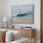 A minimalist living room features a light wood sideboard, white lamp, neutral decor, and the Lapping Tide Canvas Art—large coastal wall art with ocean waves—hung above the sideboard on a white wall.