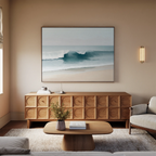 A modern living room features neutral sofas, a wooden coffee table with a small vase of flowers, a textured wood sideboard, and the Lapping Tide Canvas Art—large framed coastal wall art of an ocean wave—displayed above the sideboard.