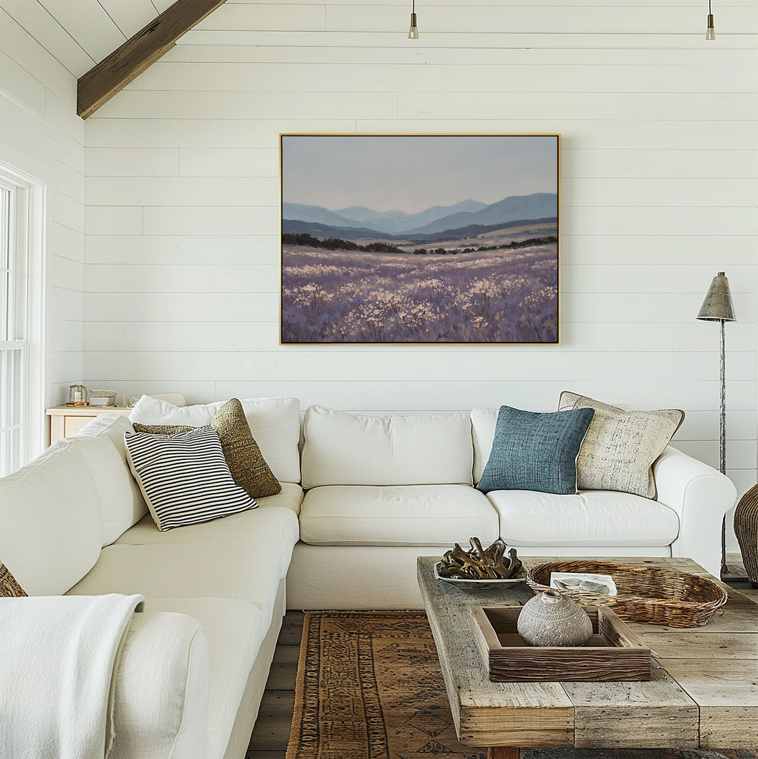 A bright, airy living room with white shiplap walls, a white sectional sofa and assorted throw pillows, a wooden coffee table, and the calming Lavender Terrain Canvas Art framed above the sofa.