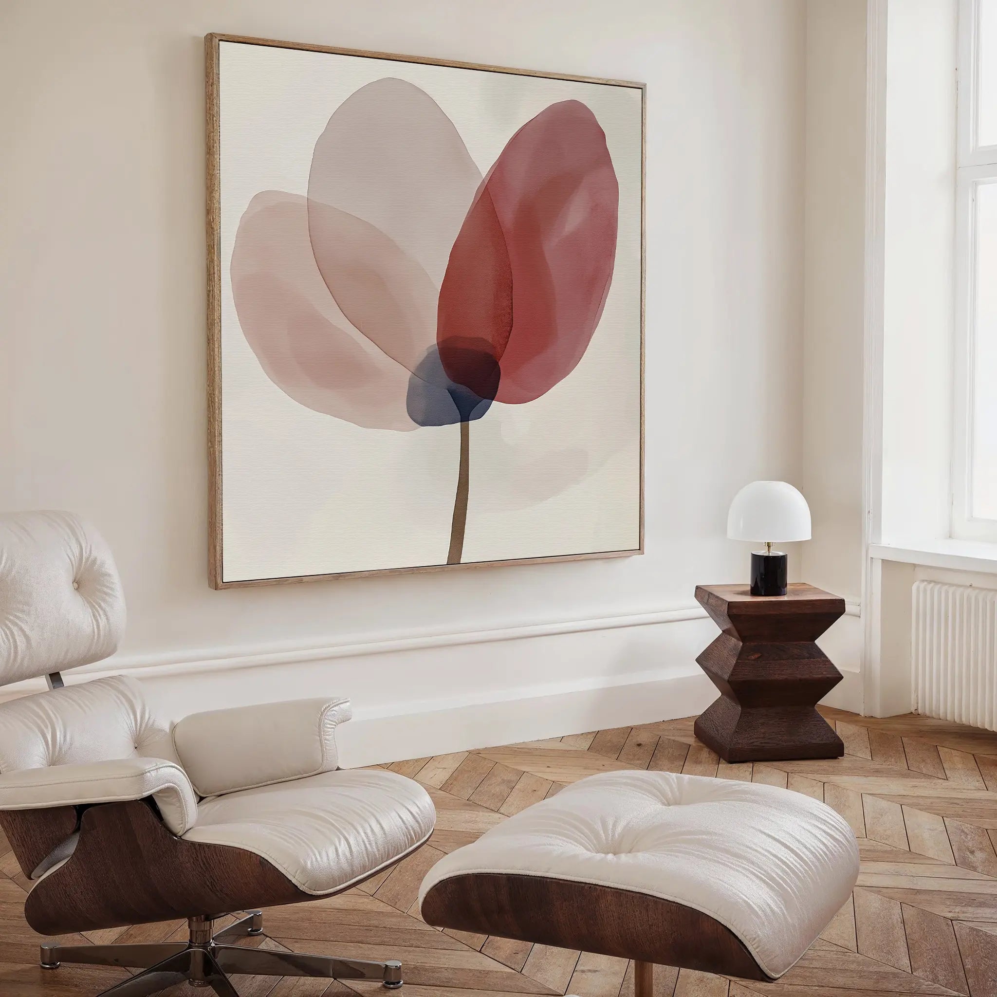 A modern living room features a cream Eames lounge chair and ottoman, a geometric wooden side table with a white lamp, and Layered Bloom Canvas Art above. Light wood chevron flooring and a tall window enhance the airy atmosphere.