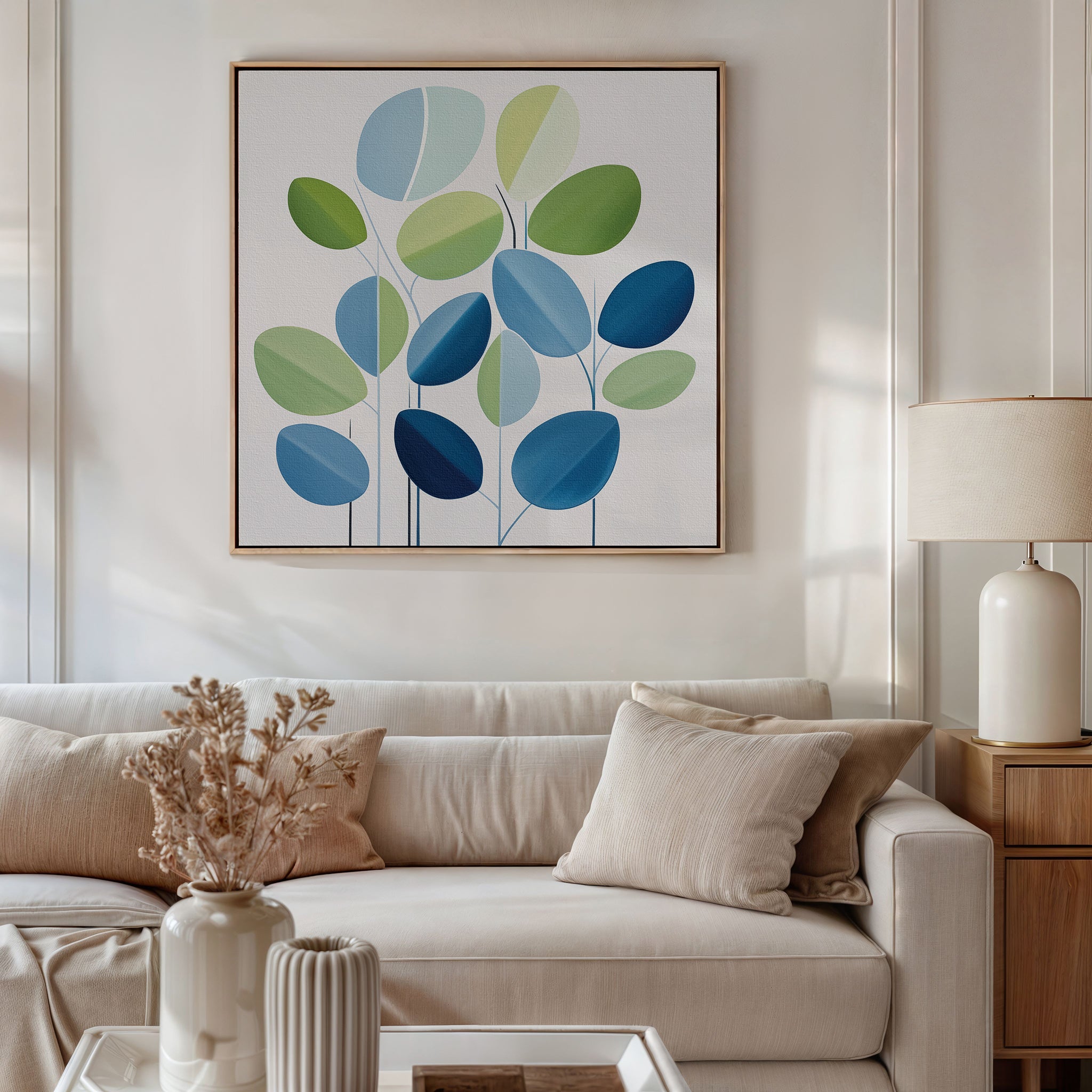 A modern living room features a light beige sofa, neutral pillows, a side table with a lamp, dried flowers in a vase, and the Layered Stillness Canvas Art—an abstract blue and green leaf painting—for stylish decor flair.