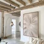 A modern, minimalist living room with exposed wooden beams, white walls, a beige sofa, and a tall arched floor lamp features the Leaf Whisper Abstract Canvas Art as a statement piece of neutral-toned wall decor.