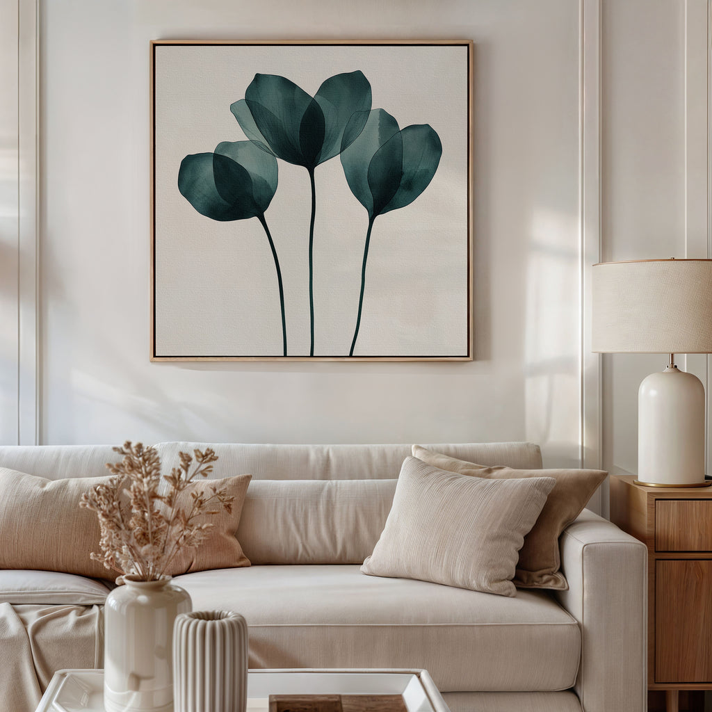A modern living room with a white sofa, beige cushions, and a side table with a lamp features the Leafy Balance Canvas Art—an abstract blue-green botanical piece. A vase with dried flowers adds charm to the room decor.