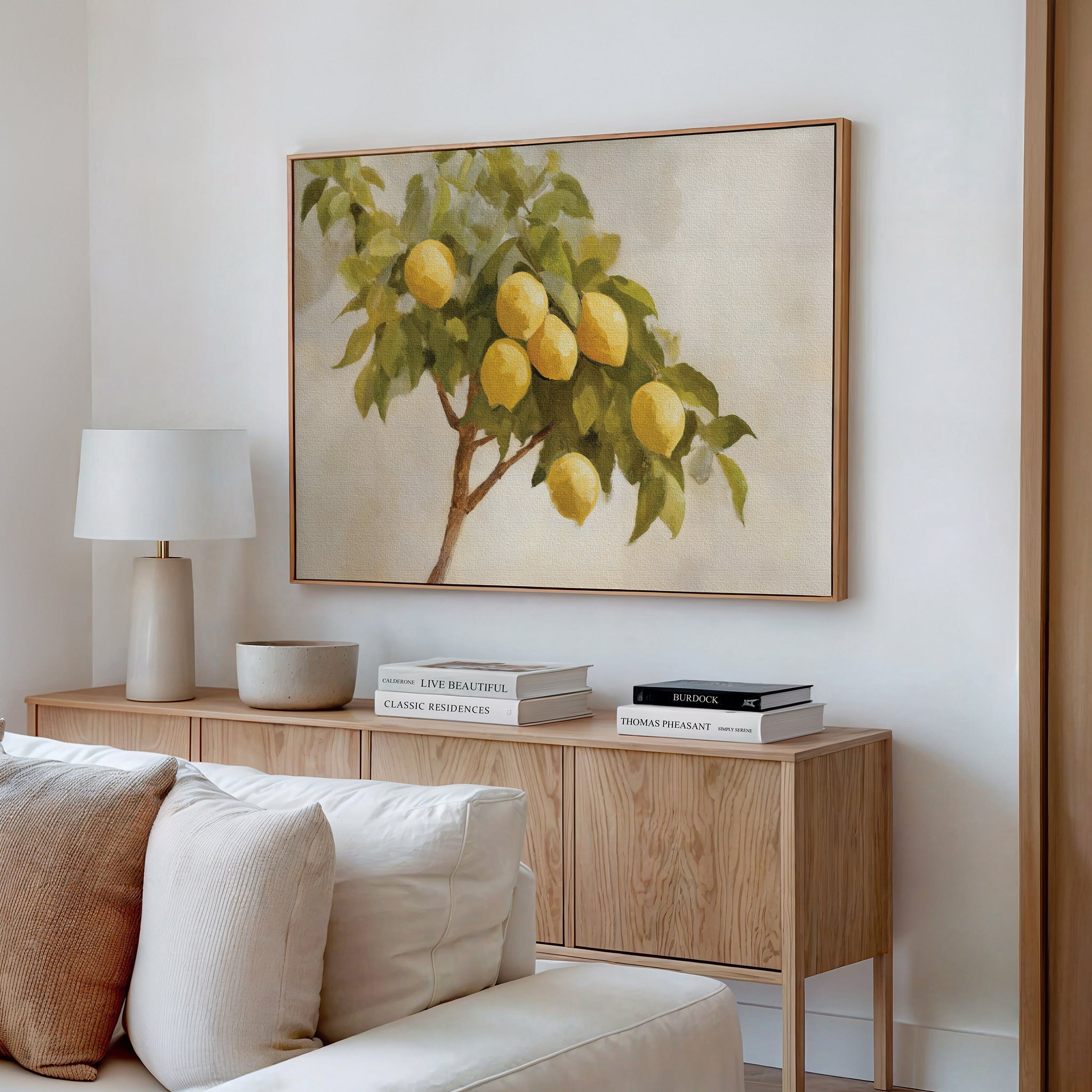 A minimalist living room features a wooden sideboard, white lamp, ceramic bowl, stacked books, and the Lemon Essence Canvas Art above. A cream sofa in the foreground enhances the serene atmosphere.