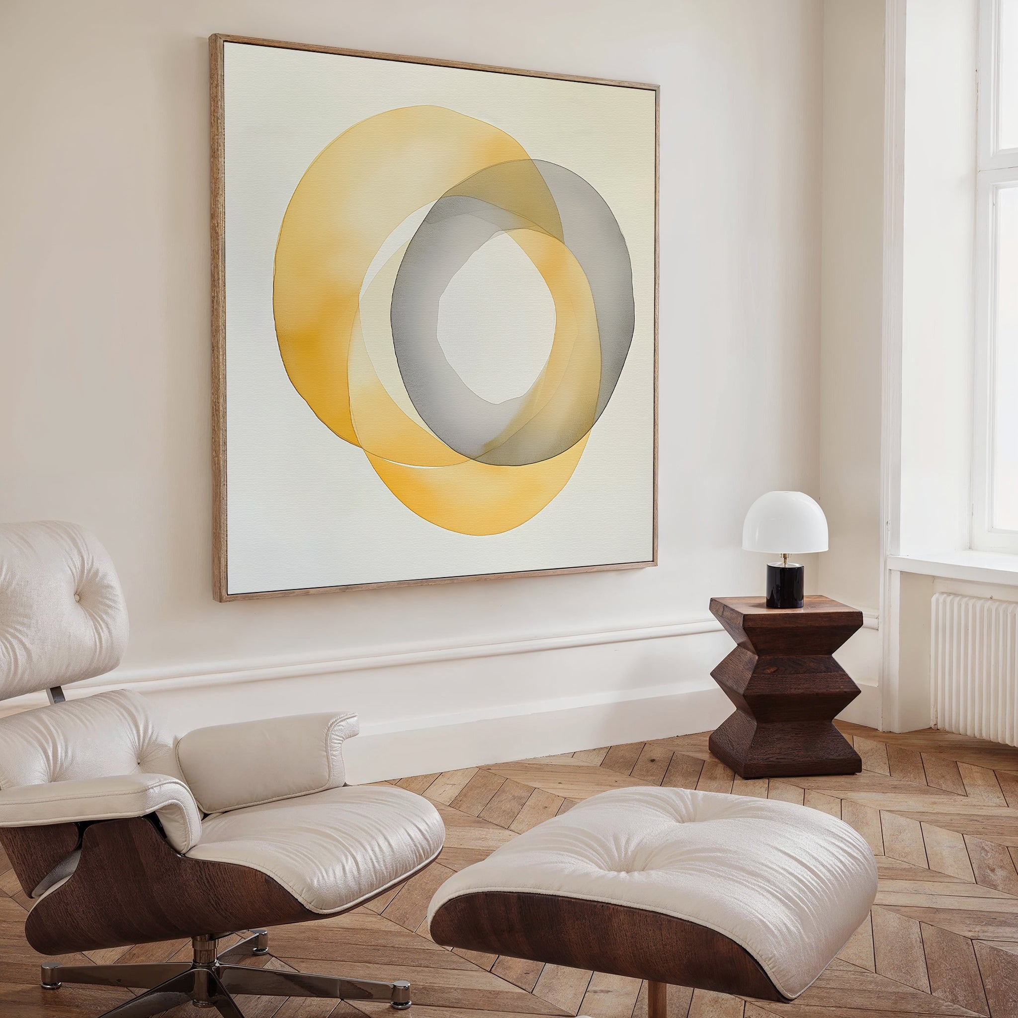 A modern living space with a cream lounge chair, ottoman, wooden floors, side table with white lamp, and striking decor featuring the Lemon Light Canvas Art—an abstract print of overlapping yellow and gray circles.
