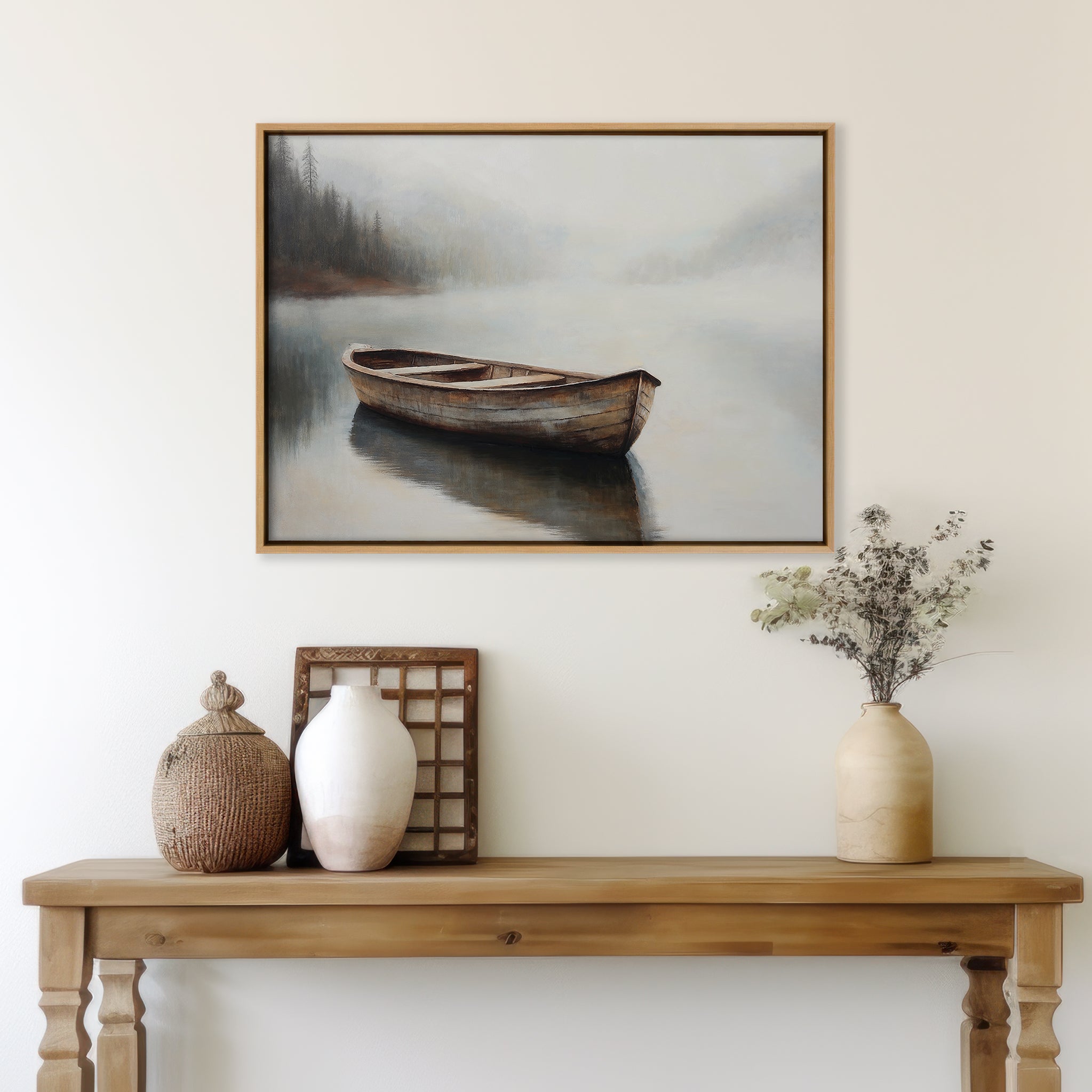 A wooden table with vases and a basket stands against a white wall, topped by Lonely Boat Canvas Art—a framed painting depicting a solitary rowboat drifting on a serene, misty lake with trees in the background.