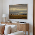 A modern living room features a wooden sideboard with books and a white lamp. Above, the Low Light Walk Canvas Art depicting a white horse in a grassy field hangs on the wall. A beige sofa sits in the foreground.