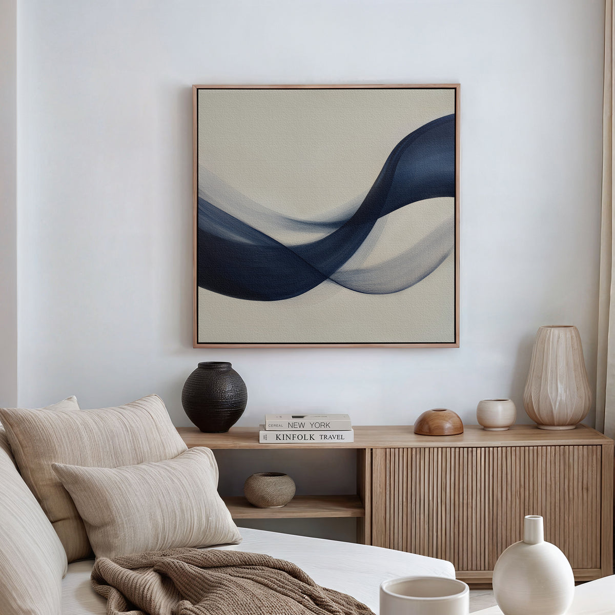 A modern living room with a neutral palette features a beige sofa, wooden sideboard, decorative vases, stacked books, and the Tidal Flow Canvas Art as minimalist wall decor.