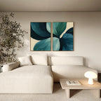 A modern living room styled with a white sectional sofa, a wooden table, a tall potted plant, and the Lush Teal Foliage Set of 2 wall art featuring abstract leaf designs in blue and green for a chic decor touch.