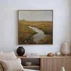 The Marshland Stream Canvas Art is framed and displayed above a light wood console with neutral decor—featuring a black vase, beige lamp, books, and a tan pillow on the sofa—in this minimalist living room.