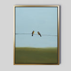 The Meadow Line Canvas Art features two small birds perched on a wire set against a blue sky and green landscape. With its minimalist style and soft colors, this framed print is ideal for modern, minimalist interiors.