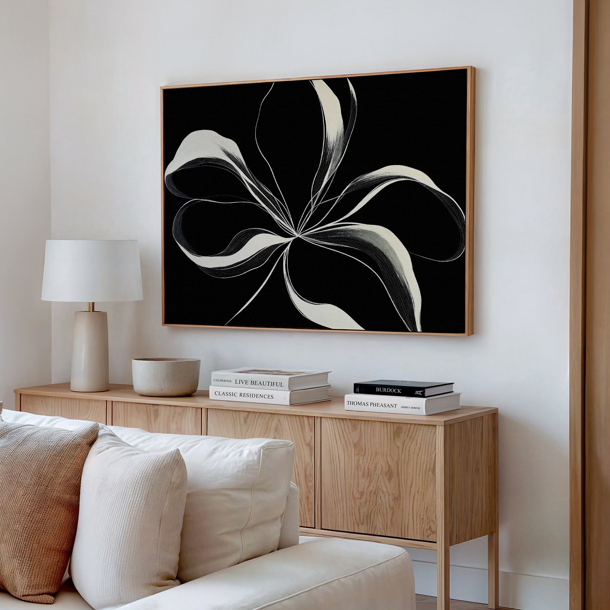 A modern living room featuring a light wood sideboard, books, a lamp, neutral decor, and the Midline Motion Canvas Art—a striking minimalist black-and-white floral painting—hanging on the wall above.