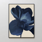 The Midnight Bloom Abstract Canvas Art features a minimalist design with a bold, stylized blue flower and layered petals on a light beige background, displayed in a frame against a white wall.