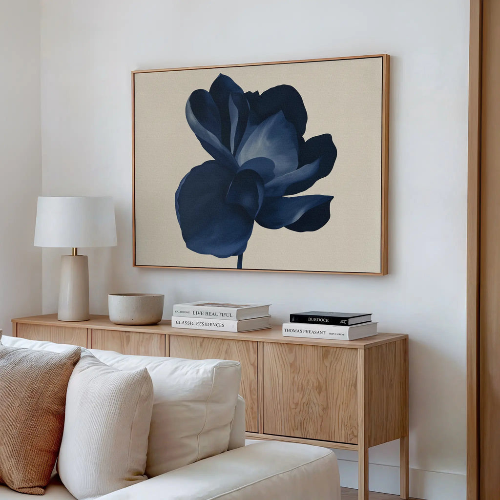 A modern living room features a light wood sideboard with books, a round lamp, and ceramics. Above it, the Midnight Bloom Canvas Art – Horizontal brings sophisticated, minimalist flair. A cream sofa sits in the foreground.