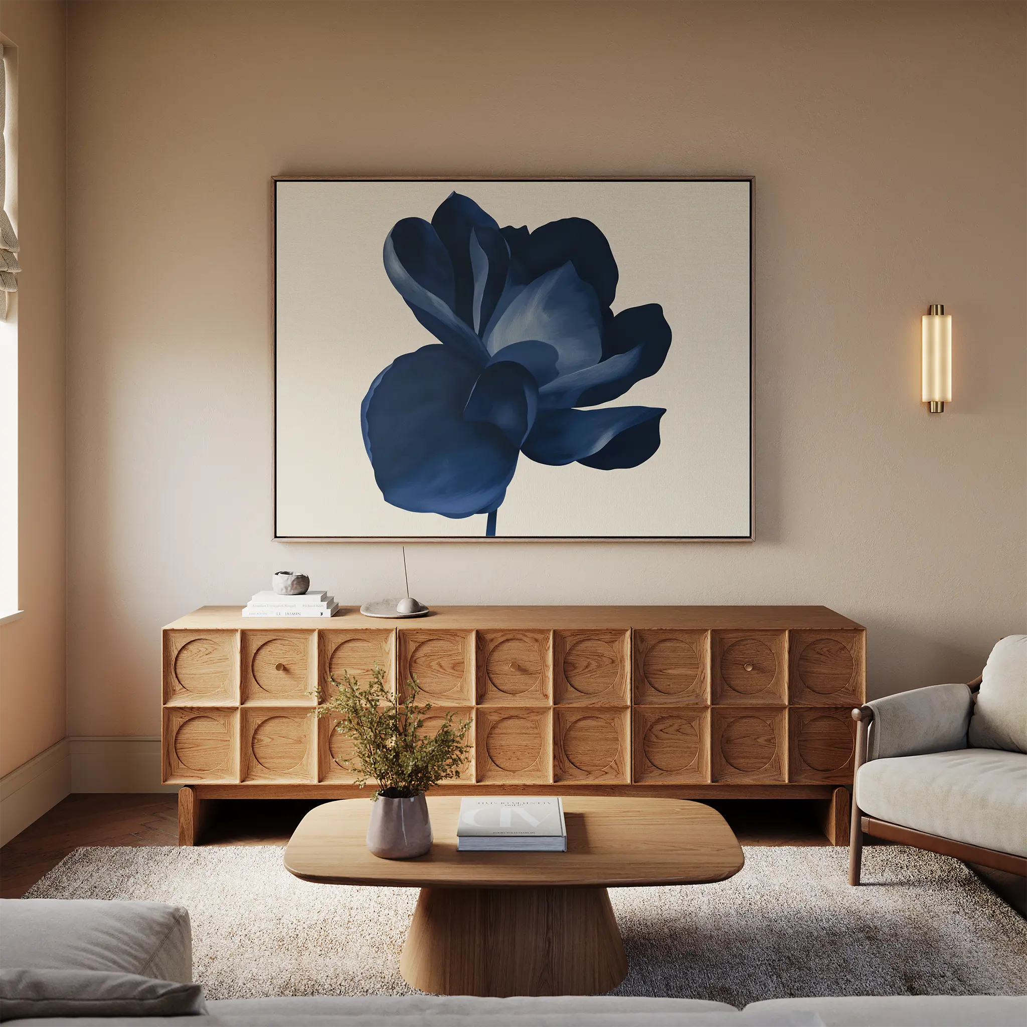 A modern living room with minimalist decor features a wooden sideboard, a light sofa, a wooden coffee table with flowers, neutral walls, soft natural lighting, and the Midnight Bloom Canvas Art – Horizontal as striking blue wall art.