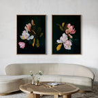 A modern living room with a curved beige sofa and round wooden coffee table displays a vase of white flowers. Above, the Midnight Blossoms Set of 2 from Nordic Park adds elegant flair to your decor with dark floral artwork.