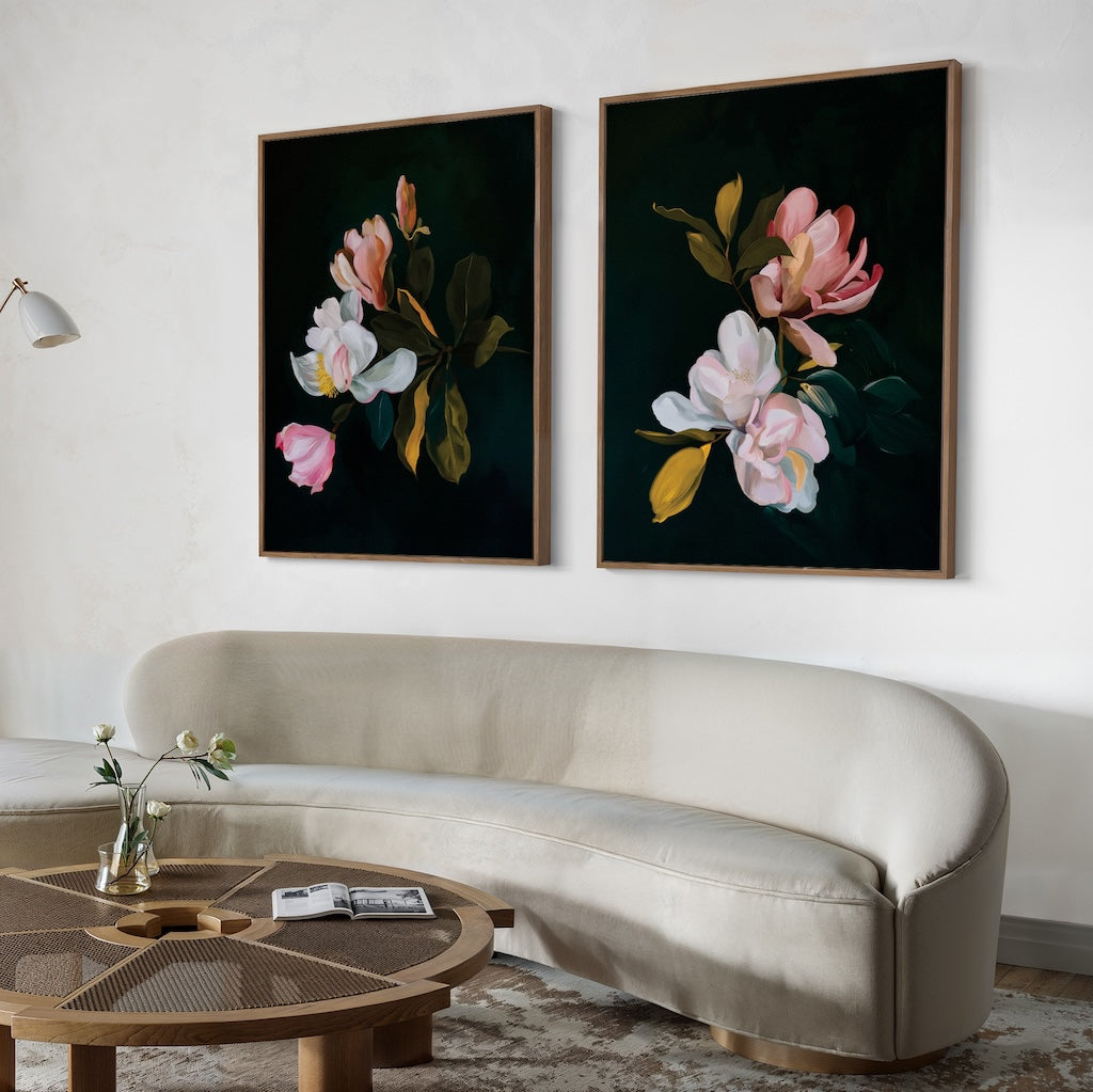 A modern living room with a curved beige sofa, a round wooden coffee table, and the Midnight Blossoms Set of 2—large framed floral paintings with dark backgrounds—for an elegant home decor touch.