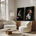 A bright living room features two modern white armchairs, a low wooden coffee table, and the Midnight Blossoms Set of 2 floral paintings on a wooden sideboard. Sunlight streams through tall windows, creating a warm, inviting atmosphere.