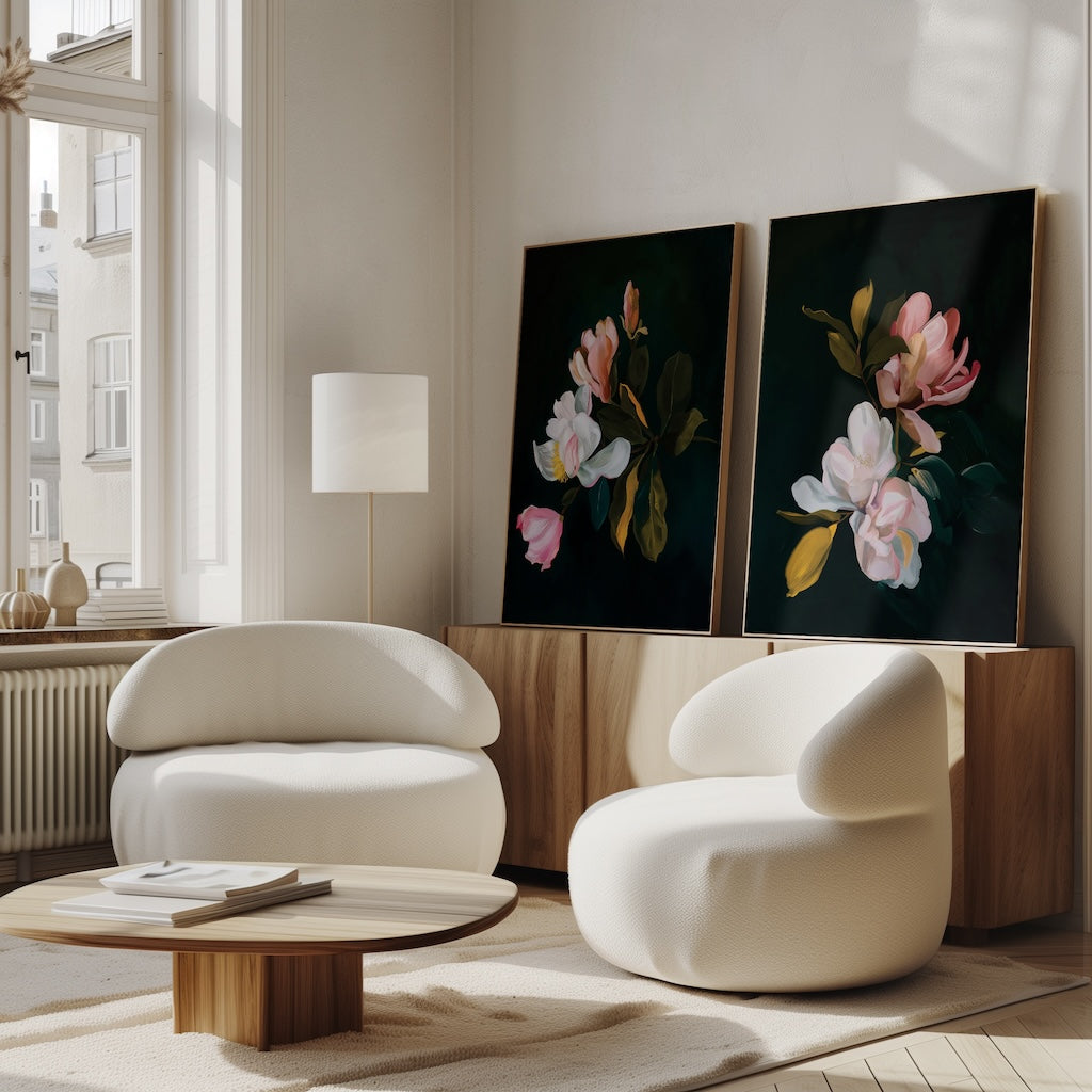 A bright living room features two modern white armchairs, a low wooden coffee table, and the Midnight Blossoms Set of 2 floral paintings on a wooden sideboard. Sunlight streams through tall windows, creating a warm, inviting atmosphere.