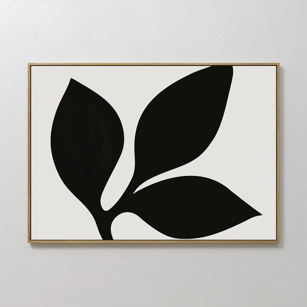 The Midnight Botanist Canvas Art features a black abstract leaf with three large leaves on a white background, framed in slim light wood—bringing modern botanical style to any living room decor.