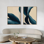 A modern living room features a curved beige sofa, a round wooden coffee table with white flowers in a vase, and two large Midnight Foliage Set of 2 abstract blue and cream artworks on the wall.