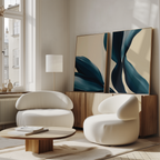 A modern living room features two rounded white armchairs, a low wooden coffee table, a sideboard, a floor lamp, large windows with streaming light, and the Midnight Foliage Set of 2 artworks for an inviting contemporary vibe.