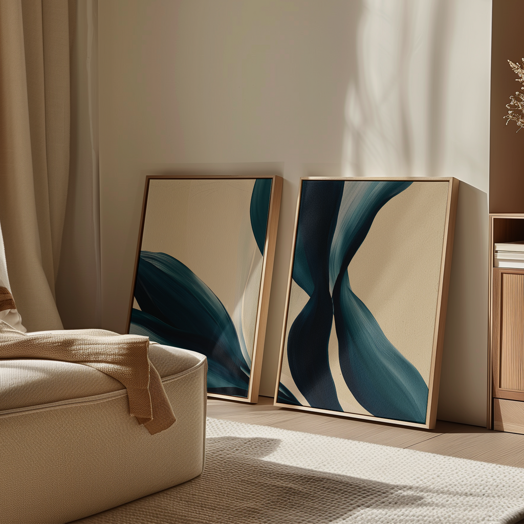 The Midnight Foliage Set of 2, featuring framed abstract art with blue and beige shapes, leans against a sunlit wall—ideal for bringing serene style to neutral spaces with soft armchairs and light wood accents.
