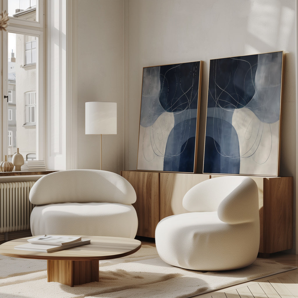 A modern living room featuring the Midnight Lines Set of 2 white curved armchairs, a low wooden coffee table, a floor lamp, and minimalist wall art on a sideboard. Sunlight streams through large windows, showcasing the room’s abstract elegance.