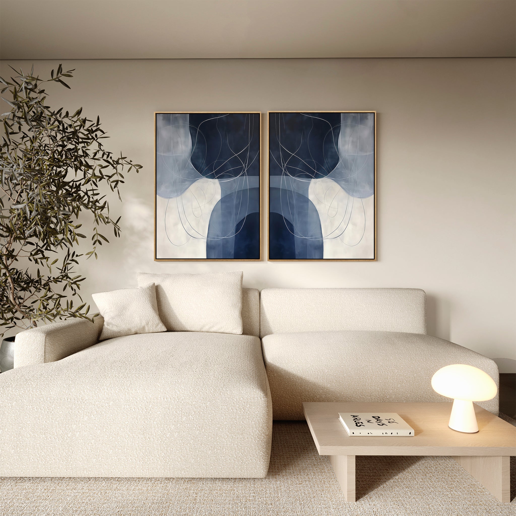 A modern living room with a cream sectional sofa, a light wood coffee table topped with a lamp and book, an olive tree, and the Midnight Lines Set of 2 minimalist wall art pieces adding contemporary elegance to the space.