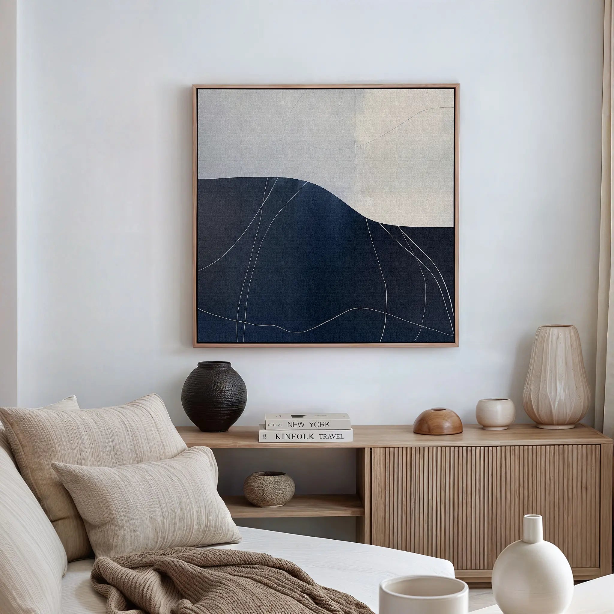 A modern, minimalist living room featuring the Midnight Terrain Canvas Art, a beige sofa with neutral cushions, a light wood cabinet, decorative vases, and books—ideal inspiration for fans of minimalist canvas decor.