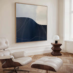 A modern living space featuring a white leather lounge chair with ottoman, a dark wood side table with a small white lamp, Midnight Terrain Canvas Art on the wall, and herringbone wooden floors for striking bedroom decor.