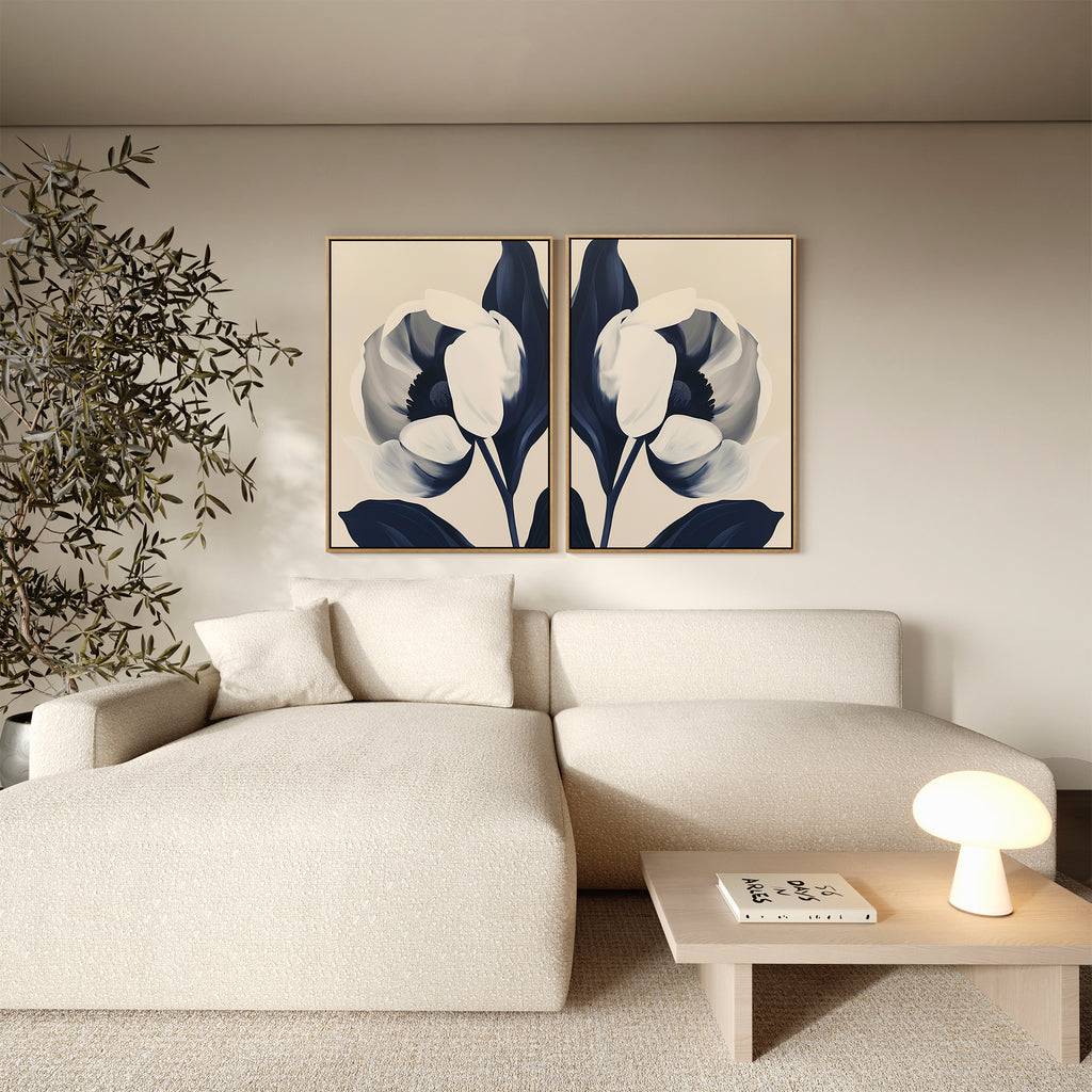 A modern living room featuring a cream sectional, a wooden coffee table, a small round lamp, a potted plant, and the "Midnight Tulip Set of 2" minimalist floral canvas prints with white and dark blue flowers as striking wall art.