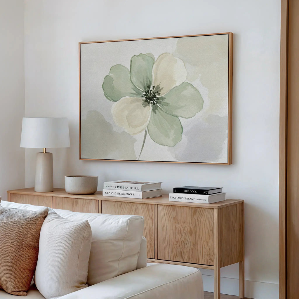 Minimalist living room with a light wood sideboard, white lamp, stacked books, small bowl, and the Mint Meadow Canvas Art featuring green and cream flowers above. A white sofa is in the foreground.