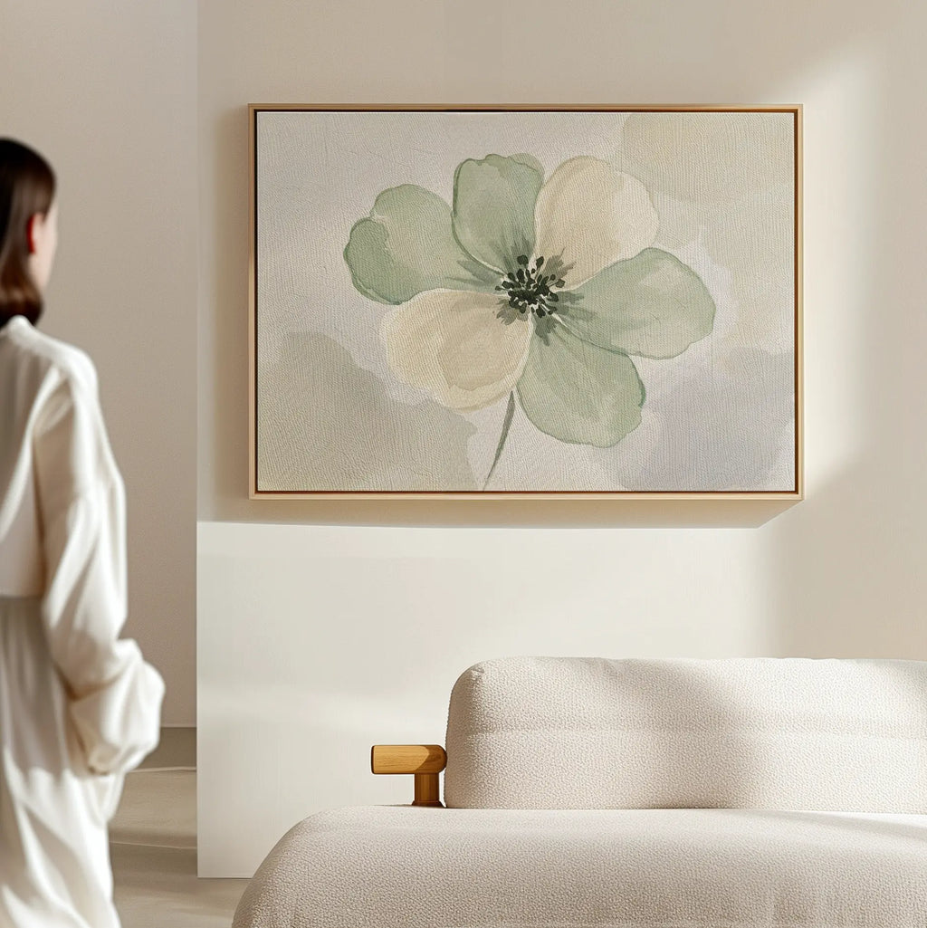 A woman in a white robe stands in a bright, minimal room, admiring the Mint Meadow Canvas Art—a large green and cream floral painting—displayed above a pale sofa.