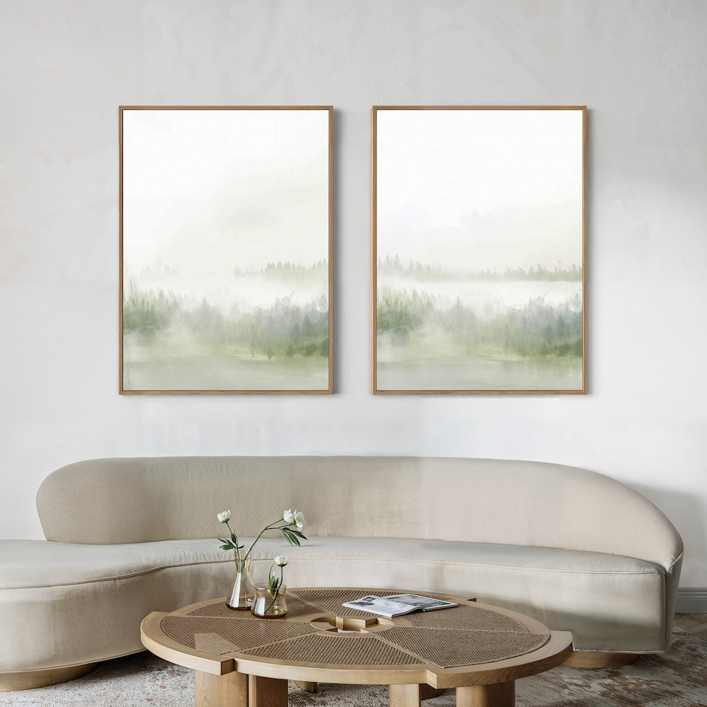 A minimalistic living room with a curved beige sofa, round wooden coffee table with a vase of flowers, and the Misty Forest Set of 2 landscape paintings above the sofa creates an inviting, serene atmosphere.