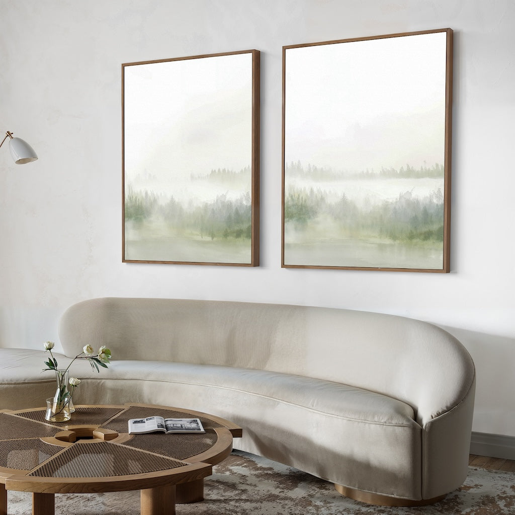 A modern living room with a curved beige sofa, round wooden coffee table, and the Misty Forest Set of 2 large framed landscape paintings creates an inviting atmosphere—ideal for inspiring SEO keywords for interior design projects.