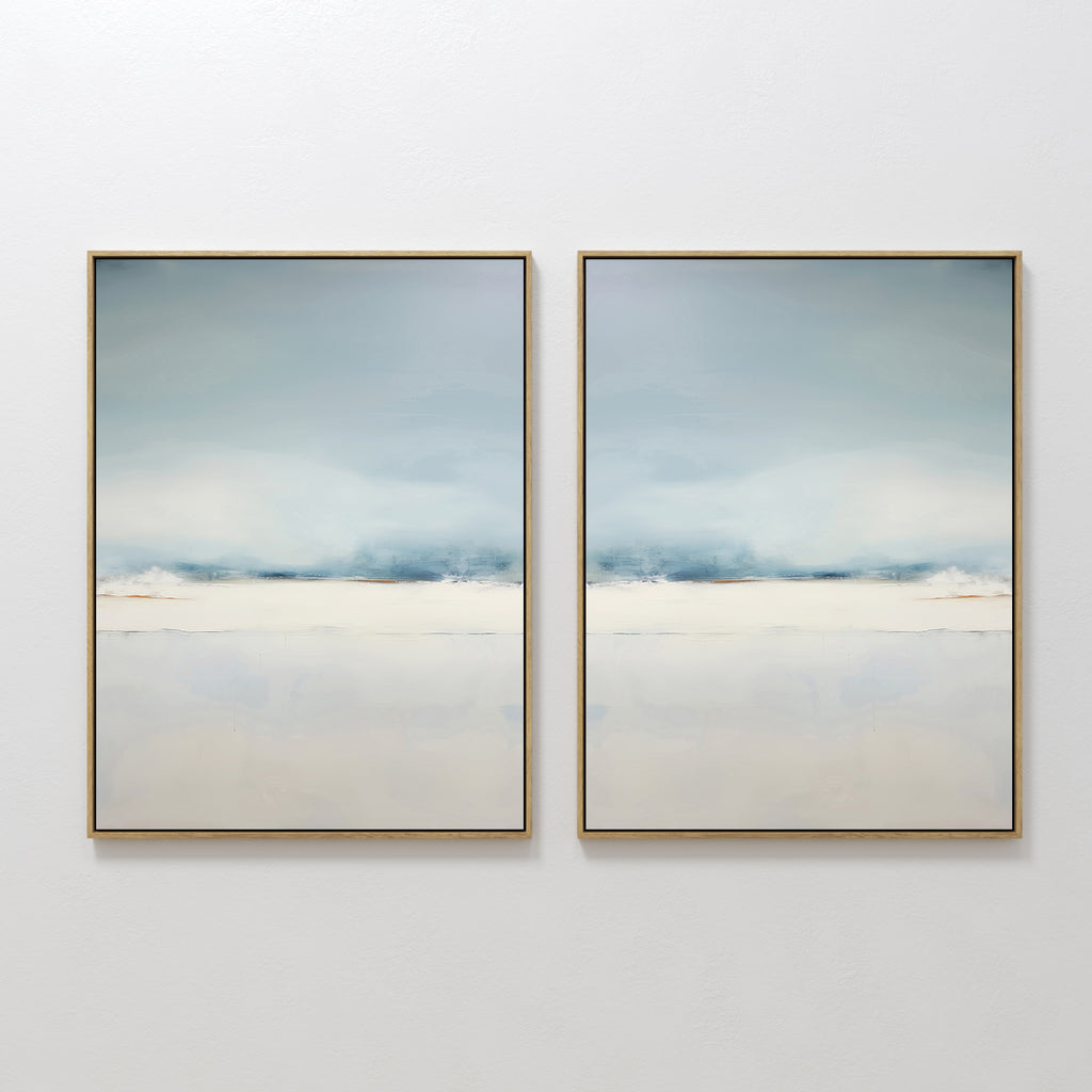 The Misty Morning Set of 2 features framed abstract paintings with soft, blurred shades of blue, white, and beige, evoking a calm sky over water. This minimalist wall art set brings a tranquil feel to any white wall.